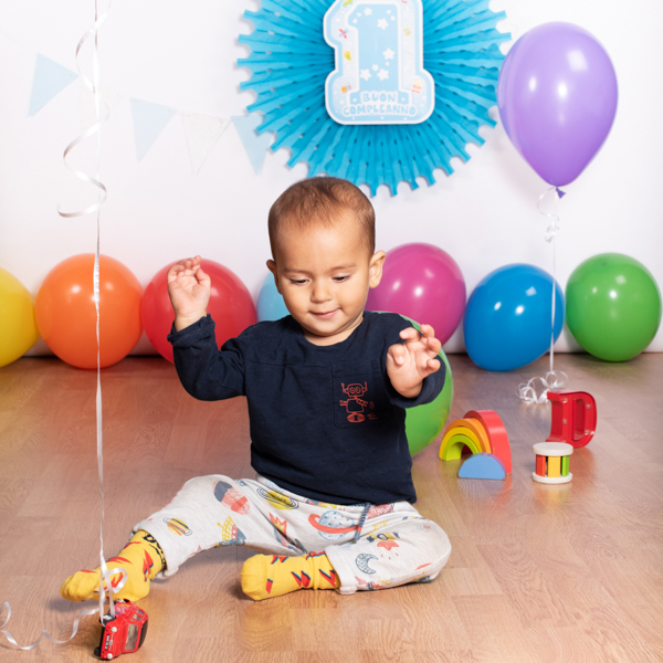foto di un bimbo al suo primo compleanno, che sorride con dei giochi e palloncini colorati