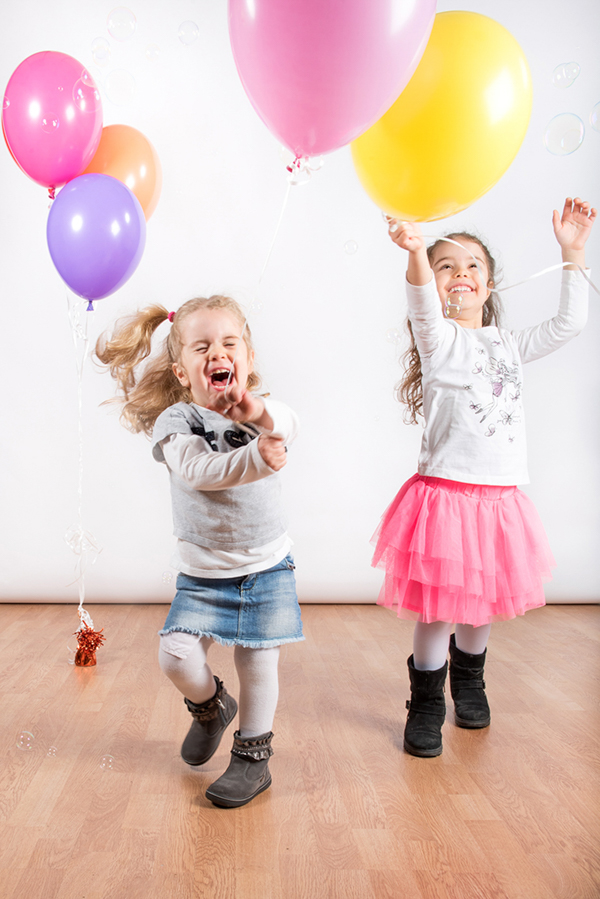 Foto di due sorelline che corrono e saltano felici giocando con i palloncini