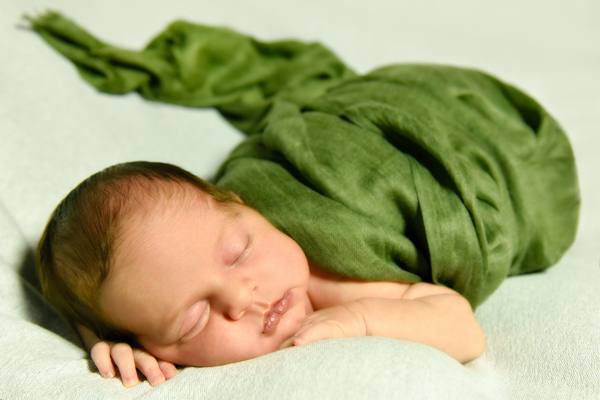Bambina appena nata che dorme con viso appoggiato sulle manine, avvolta in stoffa verde