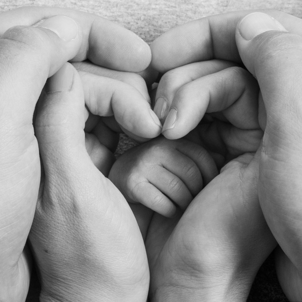 dettaglio mani dei genitori messe a cuore intorno alla manina del bimbo, bianco e nero