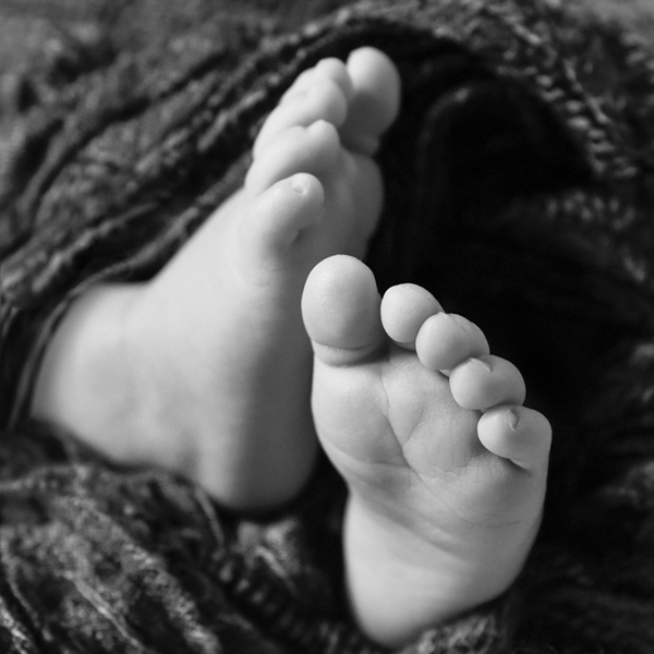 Dettaglio dei piedini del neonato avvolti in stoffa grigio scuro. bianco e nero