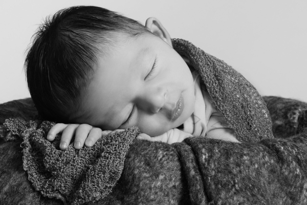 Primo piano neonato che dorme dentro a un secchio ricoperto di lana morbida. viso appoggiato sulla mano. bianco e nero