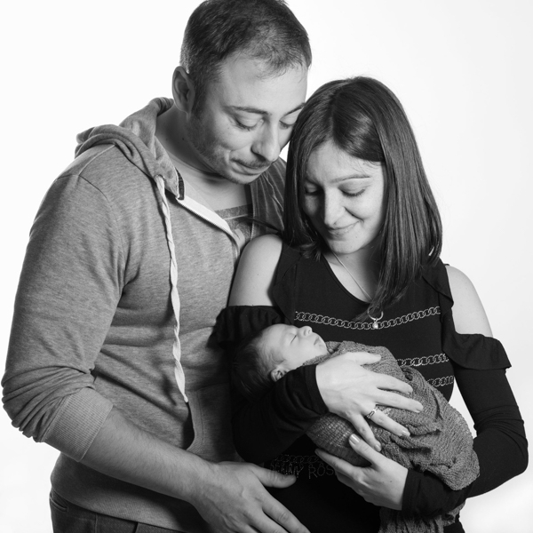 Ritratto di famiglia, con mamma che tiene in braccio la neonata e il papà che li abbraccia da dietro. bianco e nero