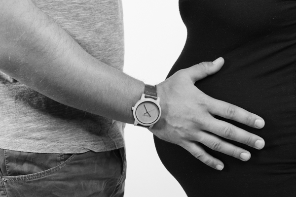 Primo piano delle pance dei genitori uno di fronte all'altro, con la mano del papà che tocca la panciona della mamma
