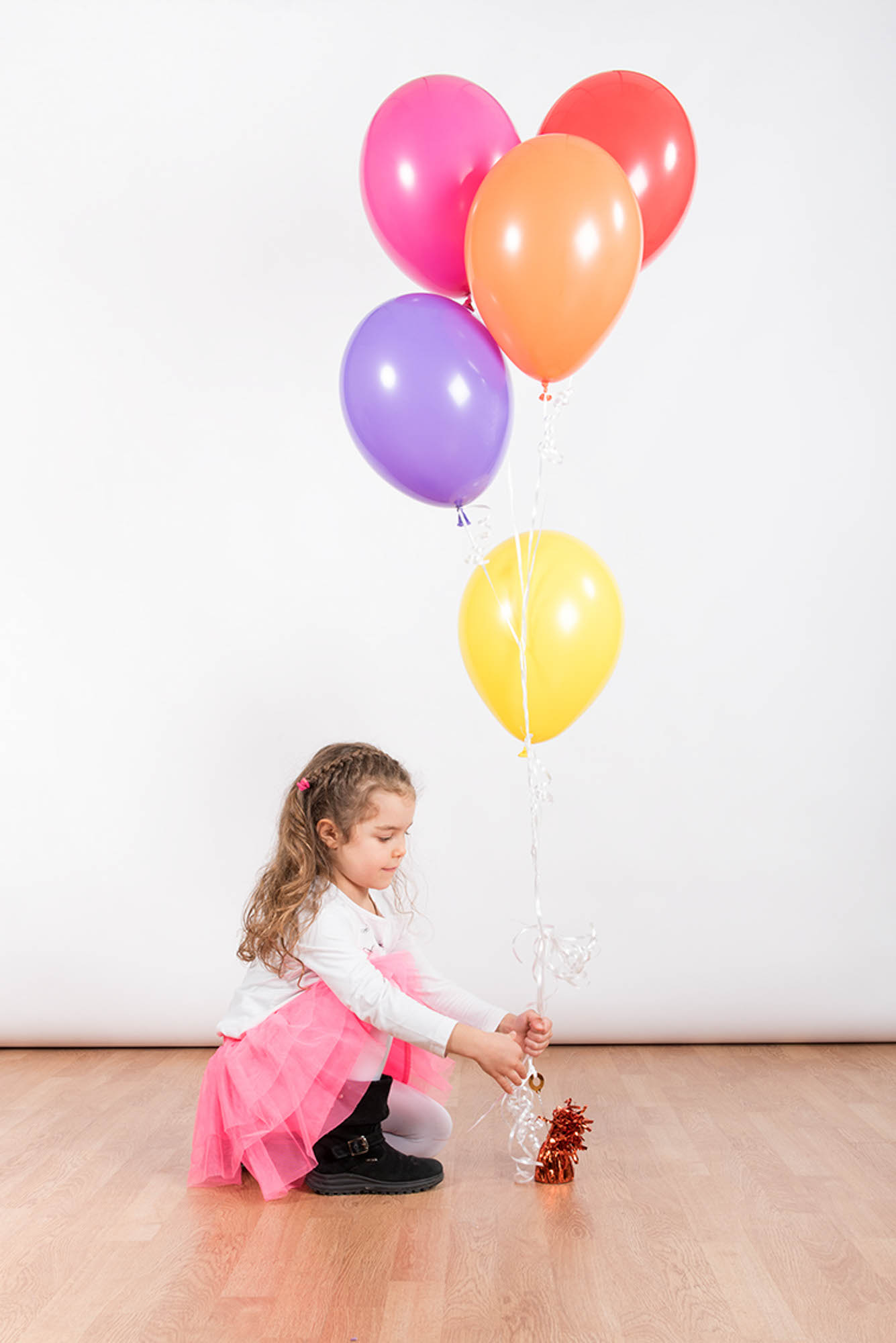 Foto di una bimba con gojnna rosa , seduta, che regge tanti palloncini colorati