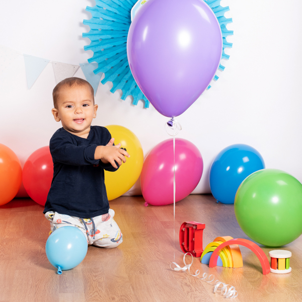 foto di un bimbo al suo primo compleanno, che sorride con dei giochi e palloncini colorati