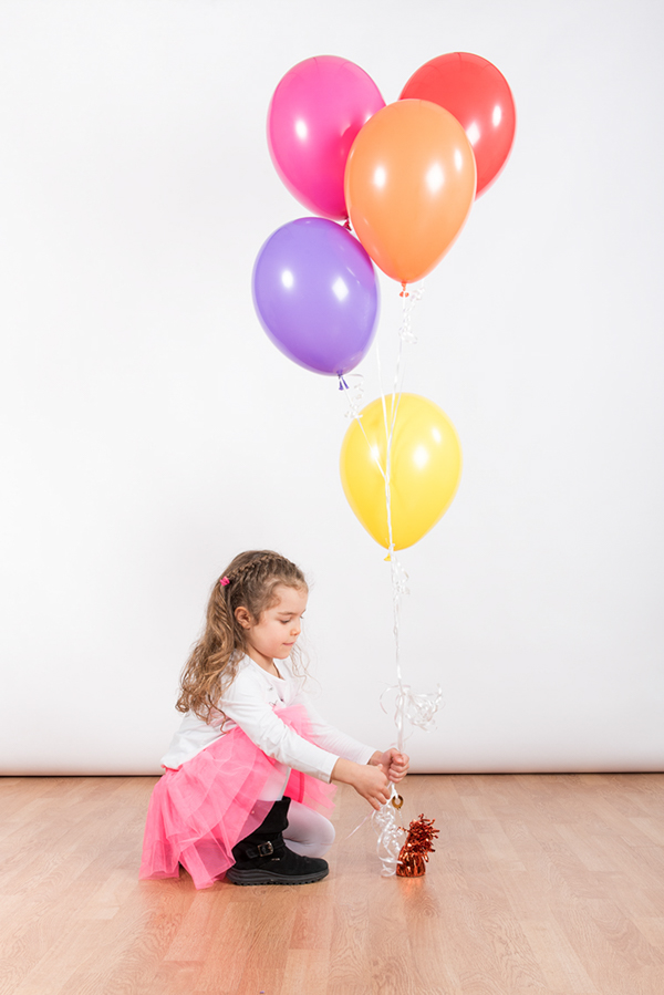 Foto di una bimba con gojnna rosa , seduta, che regge tanti palloncini colorati