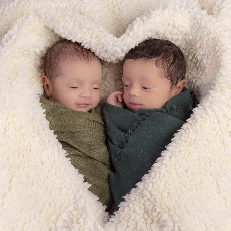 foto newborn di due gemelli con una cornice a cuore fatta con una coperta