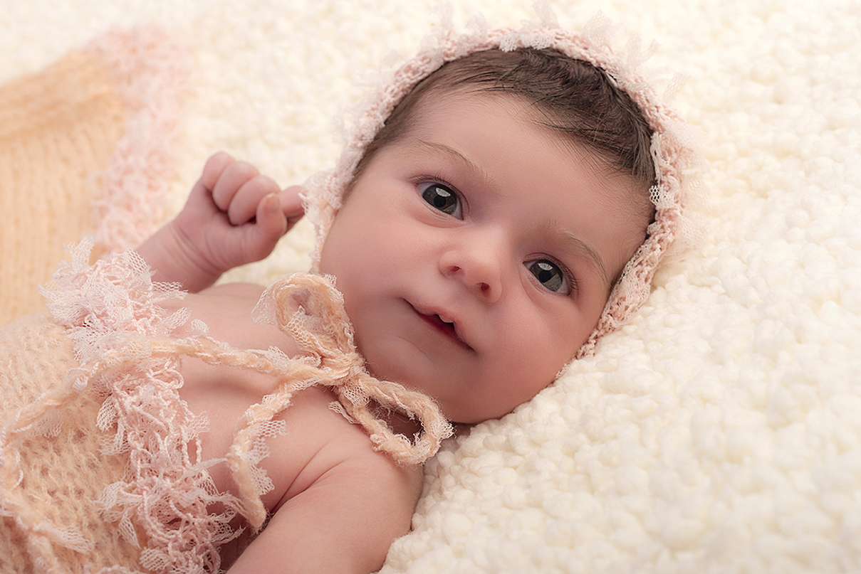 foto newborn in primo piano di una bellissima bimba con gli occhi grandi, con un cappellino di lana rosa, come la coperta