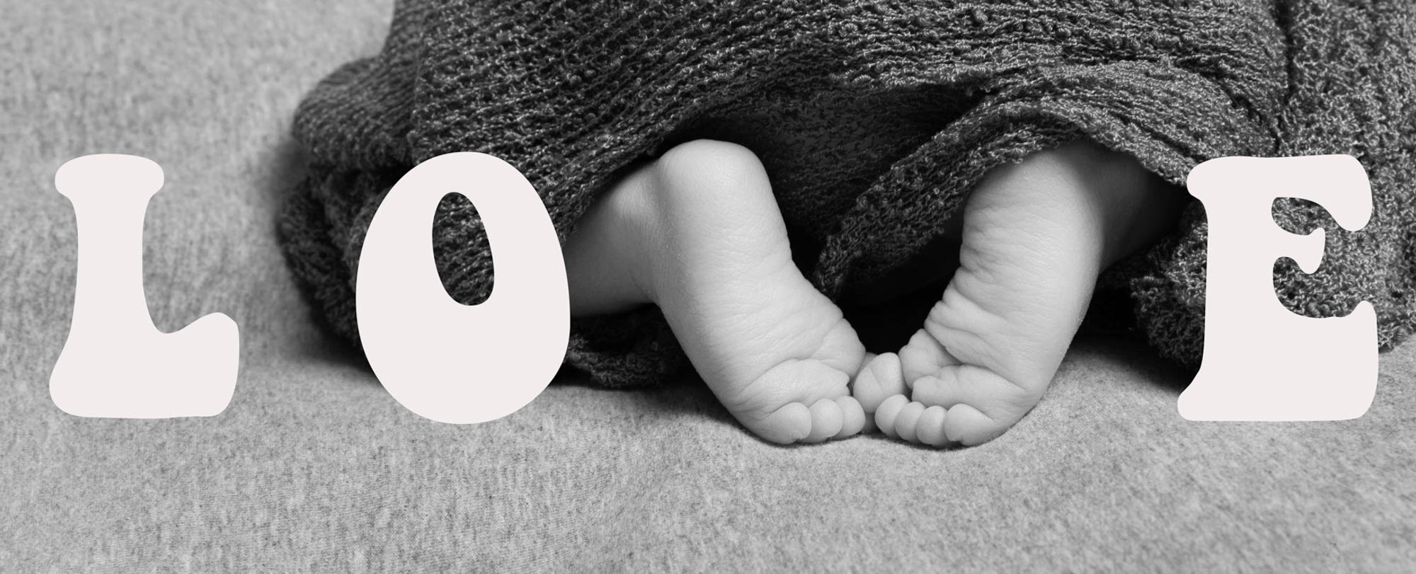 Scritta grafica LOVE con i piedini del neonato che formano la lettera V della scritta. bianco e nero
