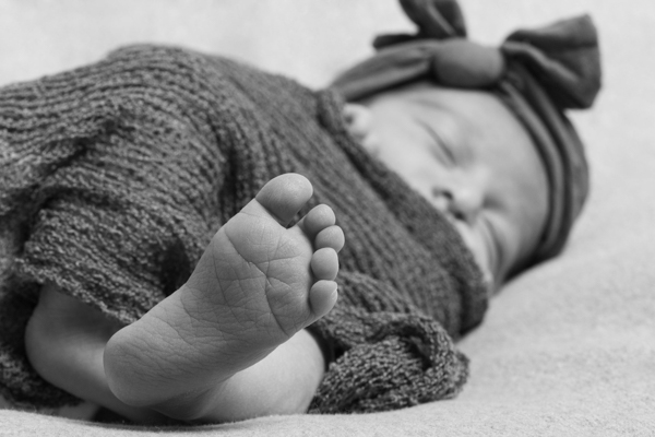 dettaglio con piedino della neonata in primo piano e il resto della bimba sfocato. bianco e nero